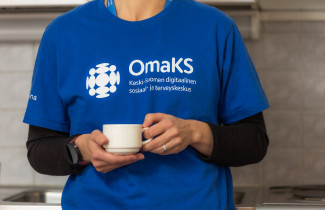 Nainen kahvikuppi kädessä OmaKS-paita päällä.